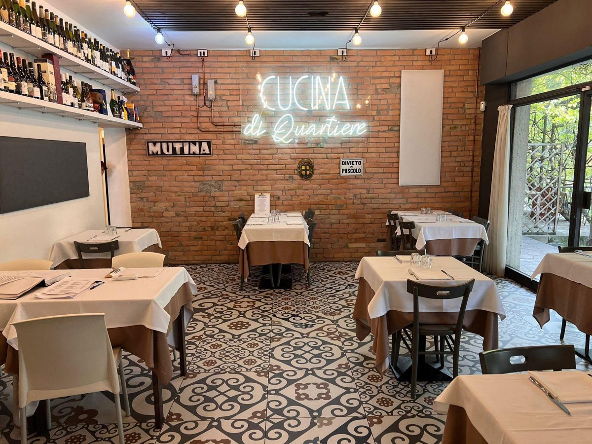La sala con l'insegna al neon Cucina di Quartiere, la scritta Mutina e le cementine a pavimento.